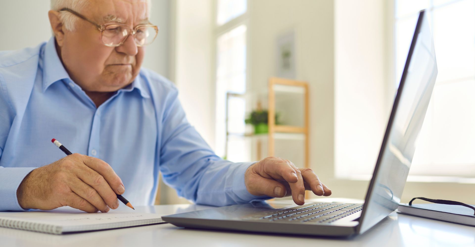 senior man looking at laptop with notepad