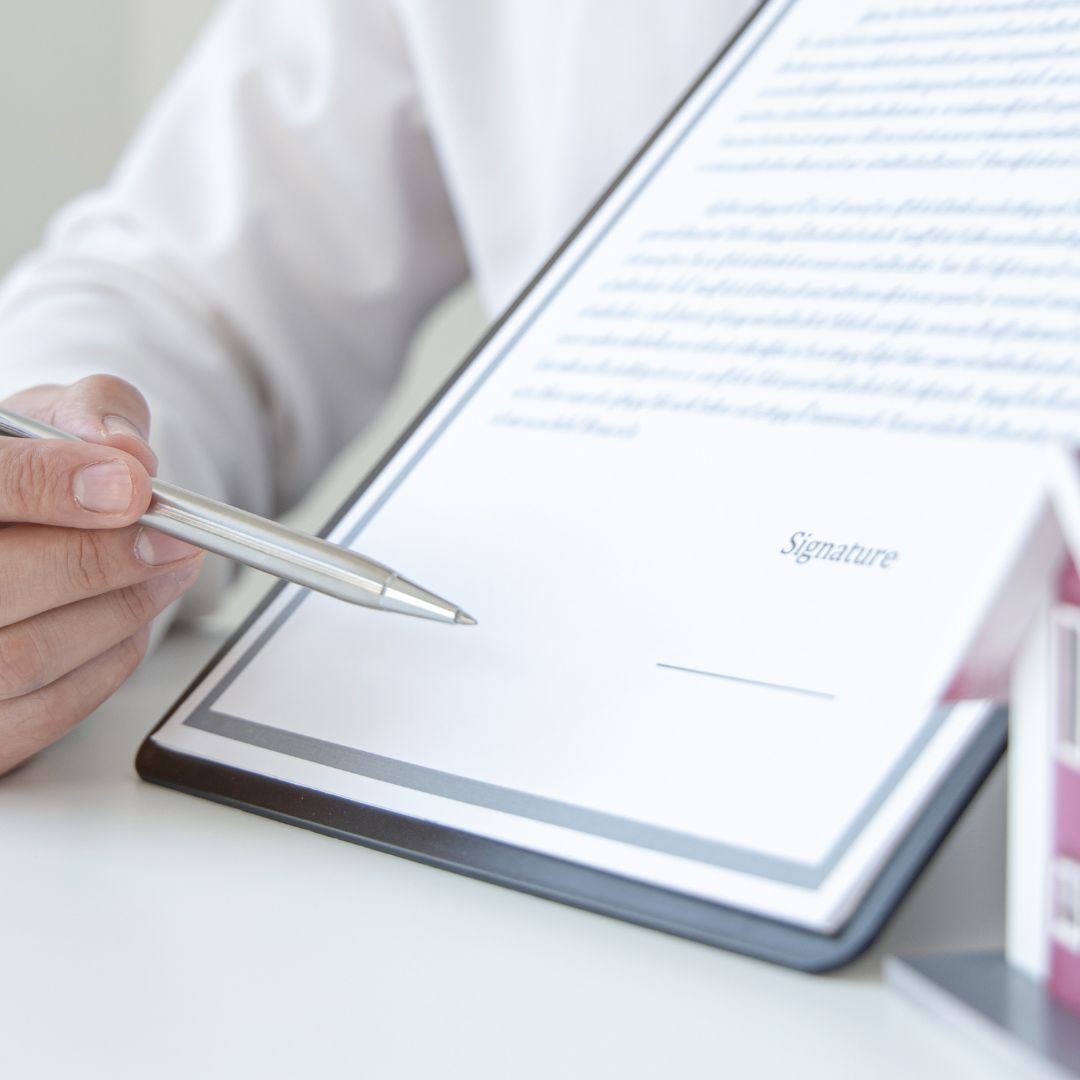 Person with a pen pointing to a signature line in a document